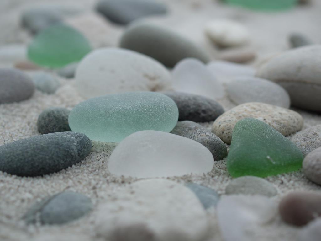 Sea glass and small smooth stones resting on pale sand